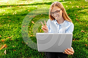 Young attractive girl in glasses, sitting with a laptop, talking on Skype and showing two fingers, on a laptop screen