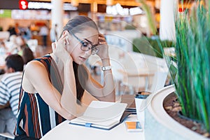 Young attractive girl in glasses uses bluetooth headset in cafe