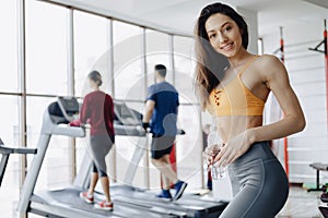 Young attractive girl in the gym drinking water on the background of treadmills