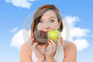 Young attractive girl holding apple and chocolate donut in fitne
