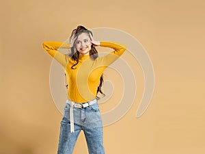 Young attractive girl with long curly hair in an orange sweatshirt holds her head with her hands on a pastel orange studio backgro