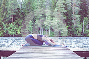 Young attractive girl practicing yoga, sitting in Child exercise, Balasana pose  on the lake. The concept of appeasement,  healthy