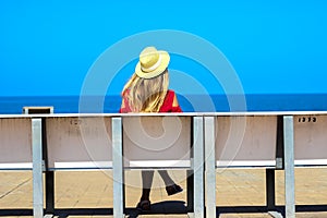 Young attractive girl in a red dress sitting on a bench near the sea in the summer, Batumi, Georgia