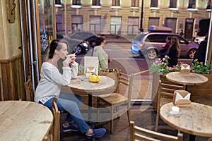 Young attractive girl sitting in the evening in a cafe with a Cup of tea to the backdrop of passing cars and city life. She looks