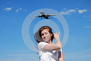 Young attractive girl smiling and posing on the background of the plane going to land on the background of the blue sky.