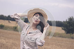 A young attractive girl in a straw hat stands in a field