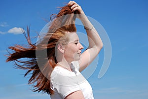 A young attractive girl throws her hair in the wind against the blue sky.