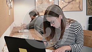 Young attractive girl is using a laptop, working with documents, making notes in the modern startup office