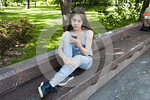 Young attractive girl waiting a call sitting on the bench. Summer park. Photo