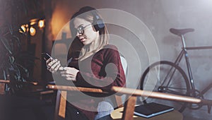 Young attractive girl wearing eye glasses and casual clothes listening digital music in headphones on smartphone at