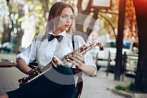 Young attractive girl in white shirt with a saxophone sitting near caffe shop - outdoor in sity. young woman with sax thinkin