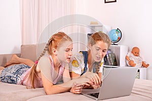 Young attractive girls  with red hair  lie on a sofa at home with a  laptop.