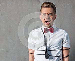 A young attractive glamorous man in a white shirt and a butterfly crocked in the microphone cord, on a gray background