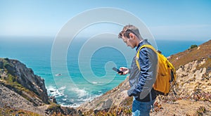 Young attractive guy with a mobile phone in his hands on the shore of the Atlantic Ocean in Portugal, Cabo da Roca