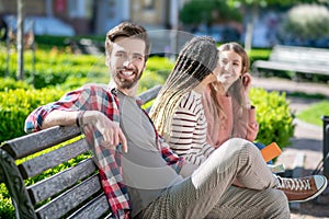 Young attractive guy posing and two girls on bench.