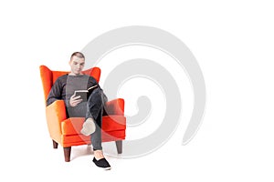 A young attractive guy is sitting on a red armchair and reading a book. Isolated on a white background. Copy space photo