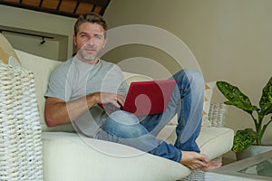 Young attractive and handsome happy man sitting at home sofa couch working with laptop computer netbook relaxed smiling cheerful i