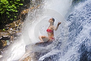 Young attractive and happy 30s woman with fit body practicing yoga wet under tropical paradise waterfall stream in meditation and