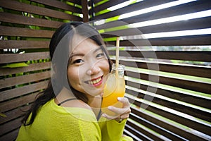 Young attractive and happy Asian Chinese girl having fun in garden outdoors drinking healthy orange juice with straw playful