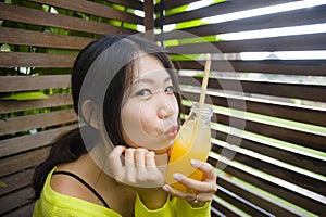 Young attractive and happy Asian Chinese girl having fun in garden outdoors drinking healthy orange juice with straw playful