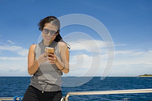 Young attractive and happy Asian Chinese woman on excursion ship or ferry using internet mobile phone smiling on holiday boat