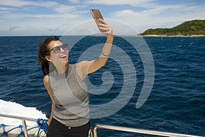 Young attractive and happy Asian Chinese woman selfie portrait picture with mobile phone on boat or ferry smiling with blue sea ba