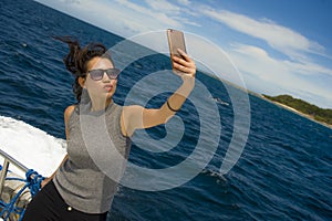 Young attractive and happy Asian Chinese woman selfie portrait picture with mobile phone on boat or ferry smiling with blue sea ba