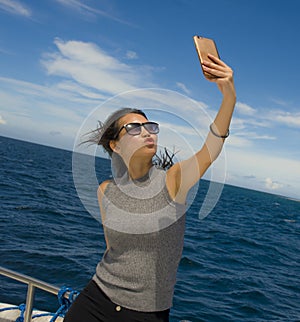 Young attractive and happy Asian Chinese woman selfie portrait picture with mobile phone on boat or ferry smiling with blue sea ba