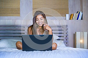 Young attractive and happy Asian hispanic ethnicity mixed woman in bed using laptop computer studying or enjoying the internet rel