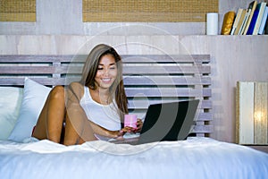 Young attractive and happy Asian hispanic ethnicity mixed woman in bed using laptop computer studying or enjoying the internet rel