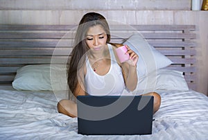 Young attractive and happy Asian hispanic ethnicity mixed woman in bed using laptop computer studying or enjoying the internet rel