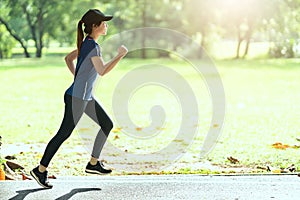 Young attractive happy asian runner woman running in public nature city park wearing sporty sportswear with copy space and sun lig