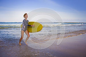 Young attractive and happy blonde surfer girl in beautiful beach carrying yellow surf board walking out of the water enjoying summ