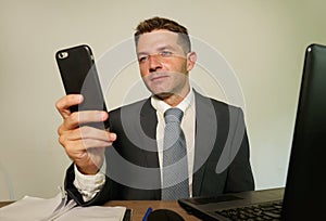 Young attractive and happy businessman in suit and necktie working on office laptop computer desk using mobile phone on isolated