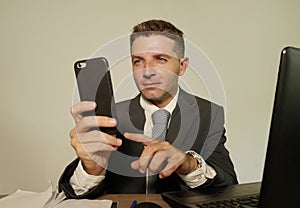 Young attractive and happy businessman in suit and necktie working on office laptop computer desk using mobile phone on isolated