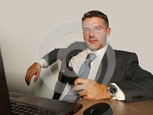 Young attractive and happy businessman in suit and necktie working on office laptop computer desk using mobile phone on isolated