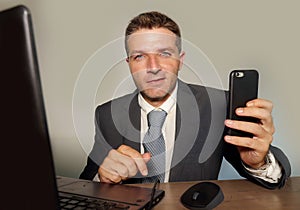 Young attractive and happy businessman in suit and necktie working on office laptop computer desk using mobile phone on isolated