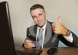 Young attractive and happy businessman in suit and necktie working on office laptop computer desk using mobile phone on isolated