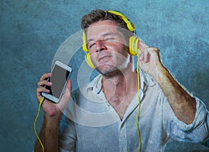 Young attractive and happy cool man listening to music song with yellow headphones using internet mobile phone dancing in trance s