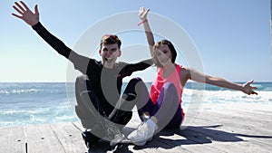 Young attractive happy couple raising the hands up in the air smiling and cheering sitting on the beach