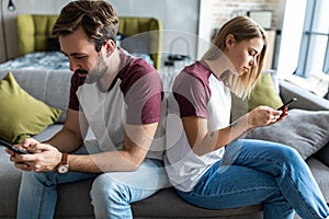 Young attractive and happy couple using internet app on mobile phone enjoying and laughing together sitting back to back at home
