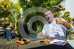 Young attractive and happy digital nomad man working outdoors from coffee shop with laptop computer giving thumb up relaxed and co