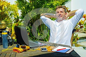 Young attractive and happy digital nomad man working outdoors from coffee shop with laptop computer leaning back relaxed and confi photo