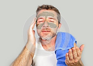 Young attractive and happy man with bathroom towel with green cream on his face applying facial mask in skin care beauty