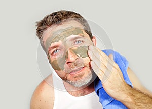 Young attractive and happy man with bathroom towel with green cream on his face applying facial mask in skin care beauty