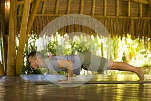 Young attractive and happy man doing yoga drill and balance exercise relaxed in harmony at beautiful Asian bamboo hut enjoying