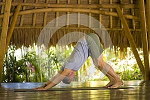 Young attractive and happy man doing yoga drill and balance exercise relaxed in harmony at beautiful Asian bamboo hut enjoying