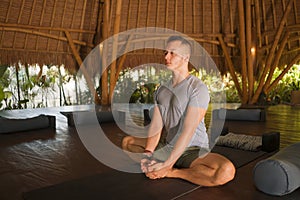 Young attractive and happy man doing yoga sitting in lotus position meditating relaxed in harmony at beautiful Asian bamboo hut