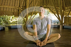 Young attractive and happy man doing yoga sitting in lotus position meditating relaxed in harmony at beautiful Asian bamboo hut
