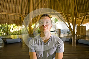 Young attractive and happy man doing yoga sitting in lotus position meditating relaxed in harmony at beautiful Asian bamboo hut